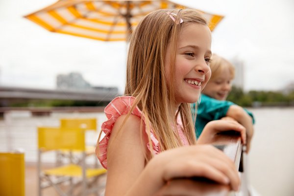 Two children are looking over the railing on the deck of a river cruise ship on the Danube, surrounded by deck chairs and sun umbrellas.