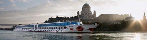 The river cruise ship A-ROSA MIA sails past Esztergom on the Danube with the St. Adalbert Cathedral at sunrise.