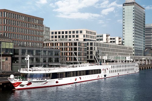 The A-ROSA SILVA is docked during the day in a port in front of modern office buildings and skyscrapers in an urban setting.