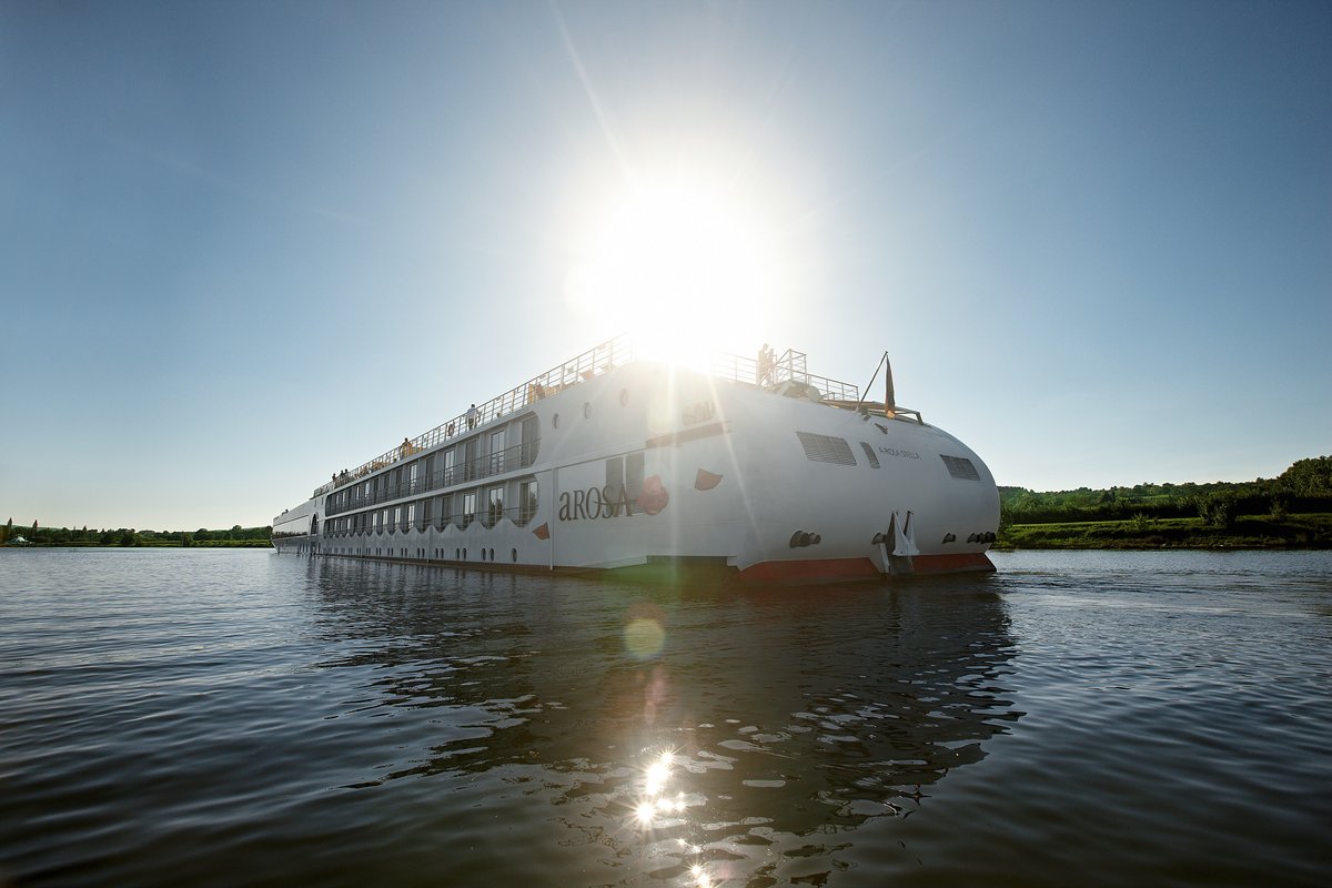 The A-ROSA STELLA photographed from behind, is sailing on the Rhône, the water is calm. The sun is shining and the sky is blue.