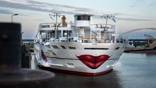 The A-ROSA SENA with a painted kissing mouth and rose on the bow is docked in the evening at a port, the sky is slightly cloudy.